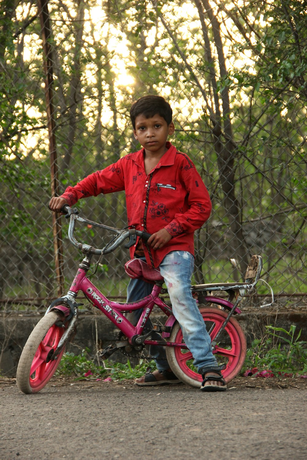 a young boy in a red shirt is riding a pink bike