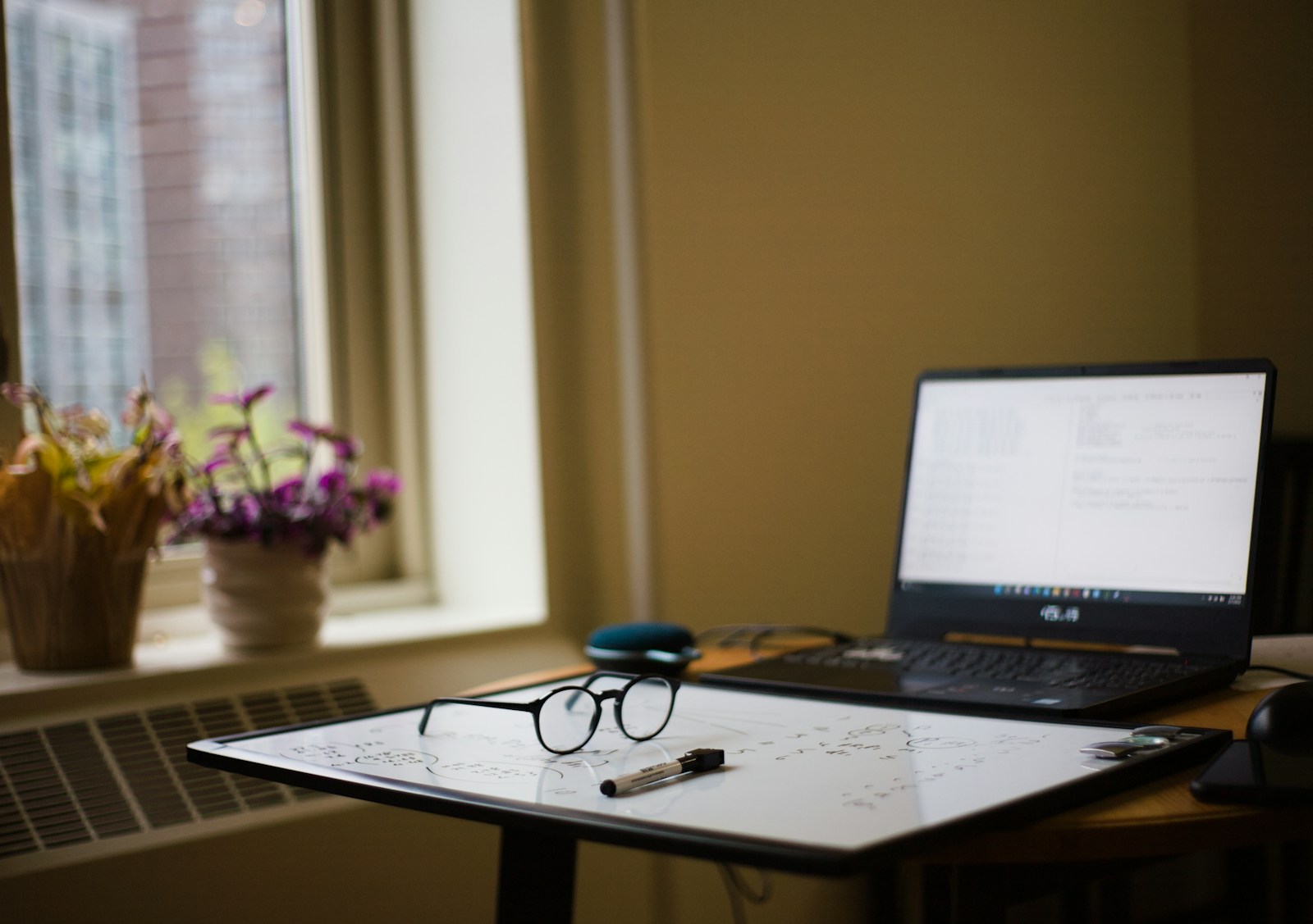 compact laptop on a small wooden desk by a window in a studio apartment