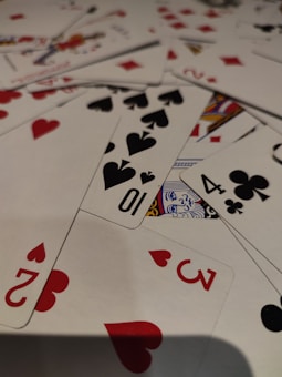 A pile of playing cards scattered across a surface, displaying a variety of suits including hearts, spades, diamonds, and clubs. Visible cards include numbers and a portion of a face card.