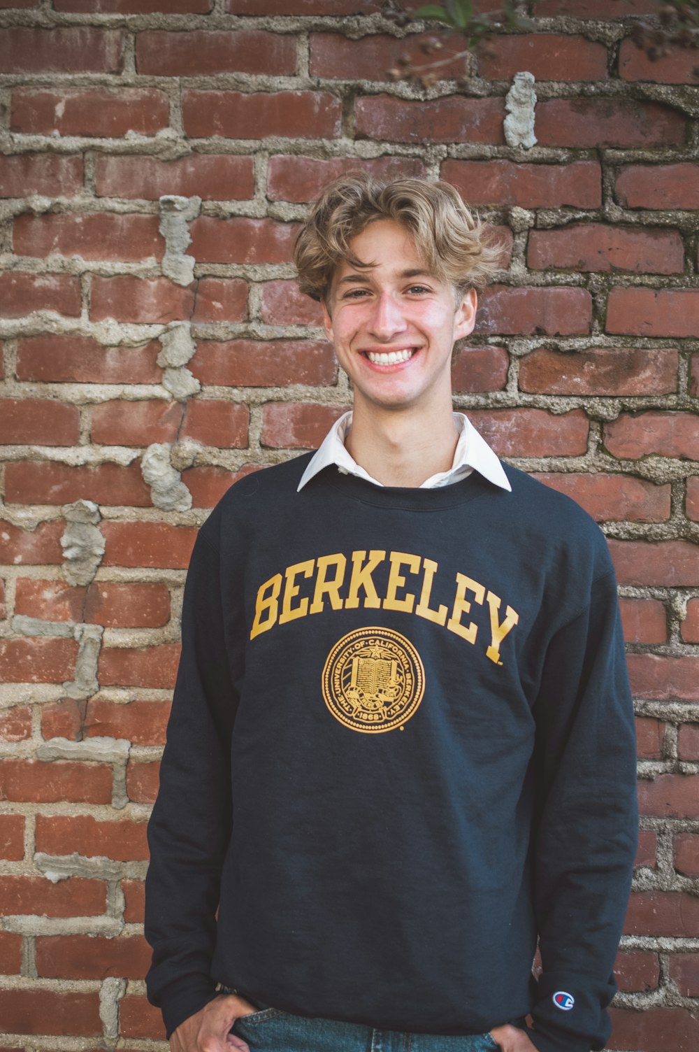 a young man standing in front of a brick wall