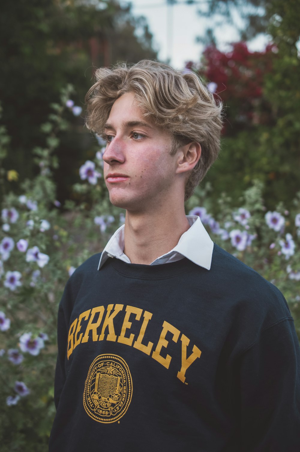 a young man standing in front of a field of flowers