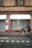 A brick building with a closed shop named Johann Schuhe, featuring two awnings above display windows covered by metal shutters. A person rides a bicycle on the road in front of the shop.