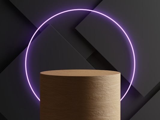 A cylindrical wooden platform is positioned in front of a modern, geometric background with overlapping dark panels. A glowing purple neon circle is centrally placed in the composition, creating a futuristic and minimalist aesthetic.