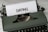 A vintage green typewriter with a piece of paper inserted, featuring the word 'DATING' typed in bold letters. The typewriter rests on a marble surface.
