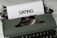 A vintage green typewriter with a piece of paper inserted, featuring the word 'DATING' typed in bold letters. The typewriter rests on a marble surface.