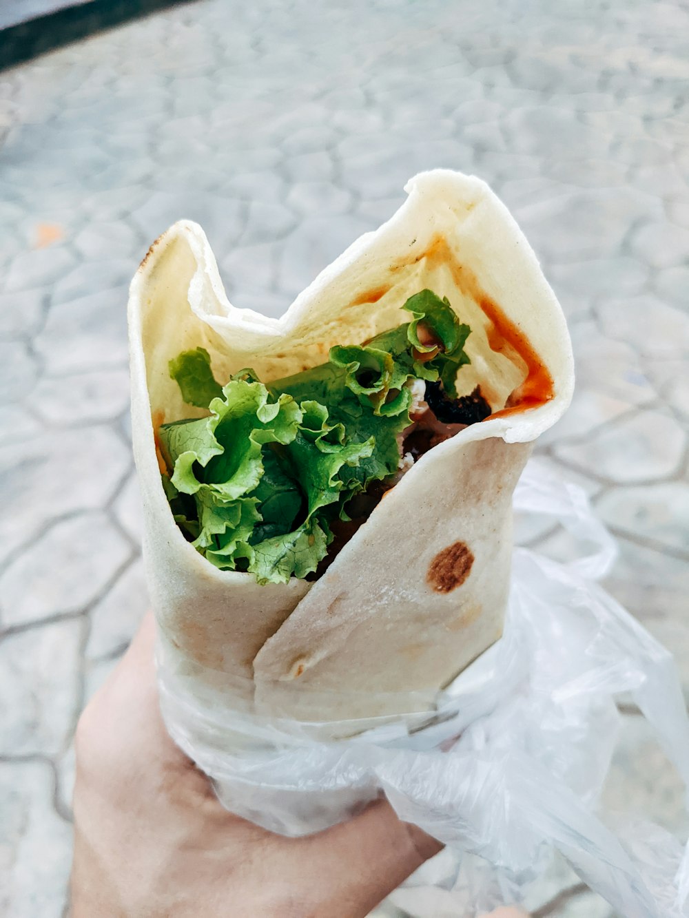 a hand holding a wrap filled with lettuce and sauce