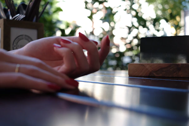 Close-up of manicured hands resting on a wooden table with rosewood accents.