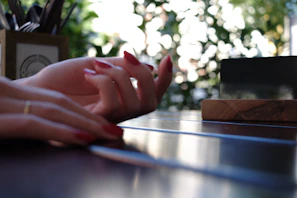 Close-up of glossy, vibrant red press-on nails with delicate gold accents on a wooden table.