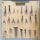 A pegboard is neatly organized with various tools, including scissors, pliers, hammers, and other hand tools. Each tool is secured on the board with a white strap. At the top, a label reads 'TOOLS OF THE TRADE'. The arrangement is symmetrical and orderly, with tools of different shapes and sizes.