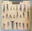 A pegboard is neatly organized with various tools, including scissors, pliers, hammers, and other hand tools. Each tool is secured on the board with a white strap. At the top, a label reads 'TOOLS OF THE TRADE'. The arrangement is symmetrical and orderly, with tools of different shapes and sizes.