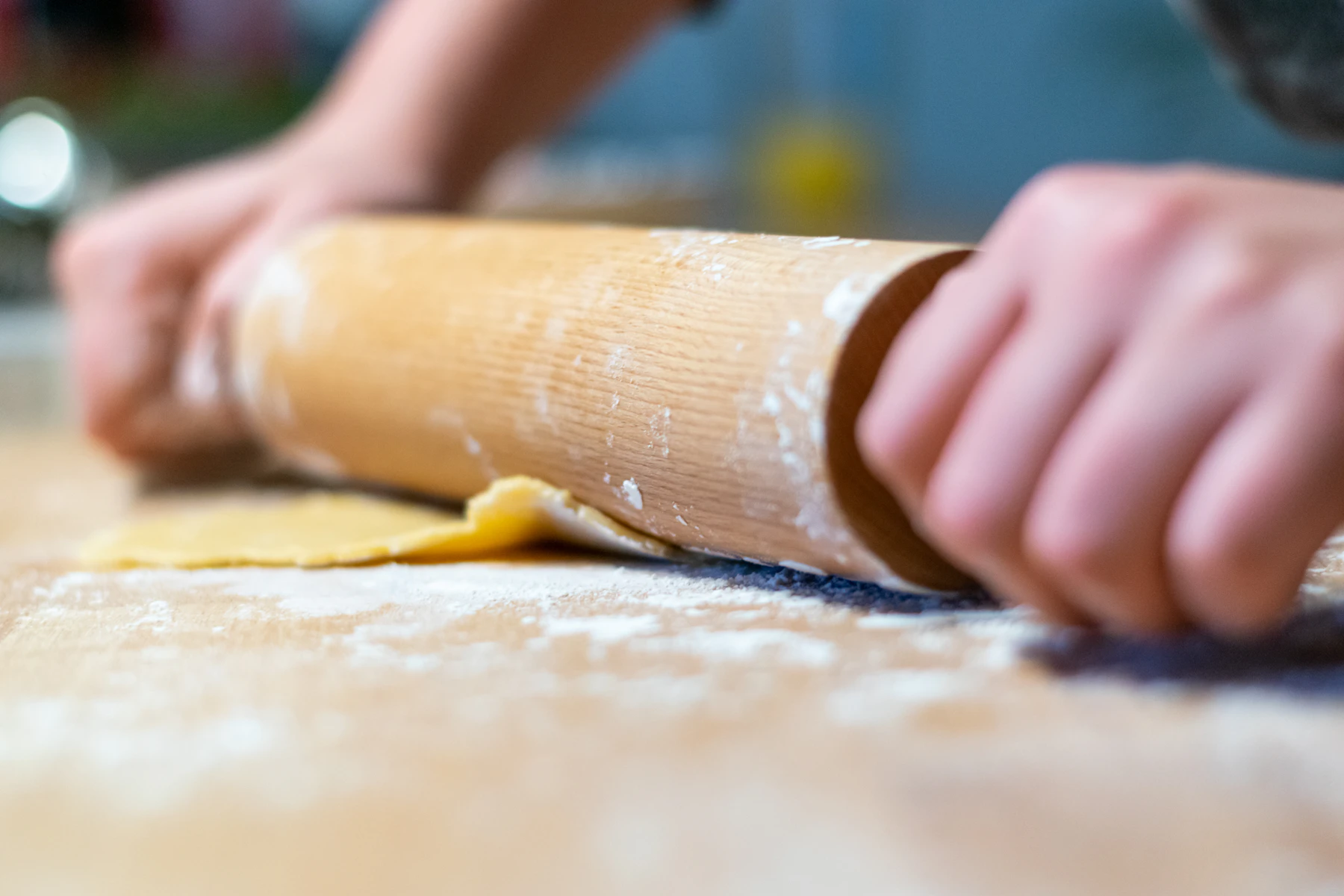 Hands pushing a wooden rolling pin over thin pastry dough on a floured board