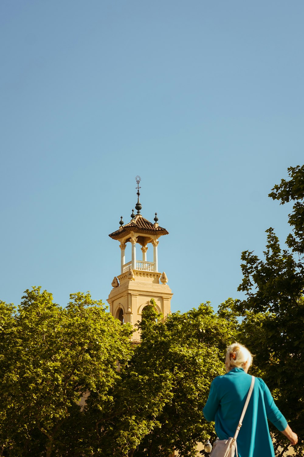 a woman in a blue top is walking towards a clock tower
