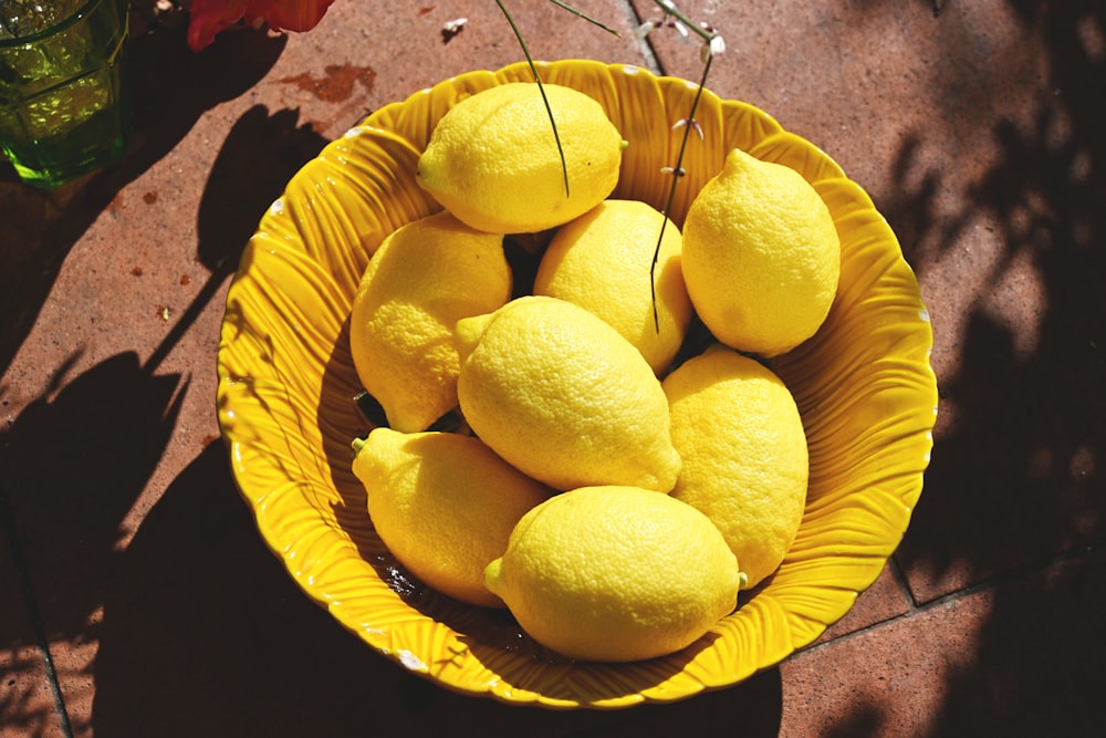 a yellow bowl filled with lemons on top of a table