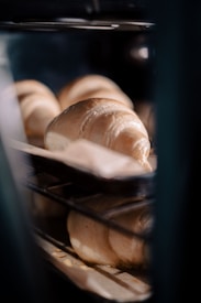Several croissants are baking inside an oven. The croissants are placed on baking trays and are in the process of rising and turning golden brown. The image is taken through the oven door, giving a close-up view of the croissants.