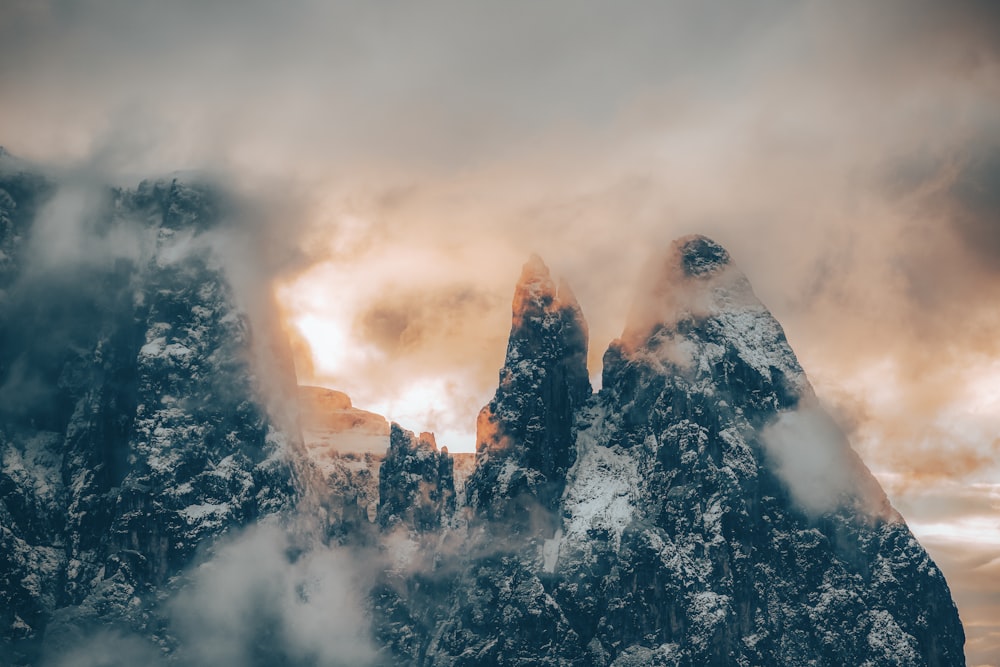 a mountain covered in snow and clouds under a cloudy sky