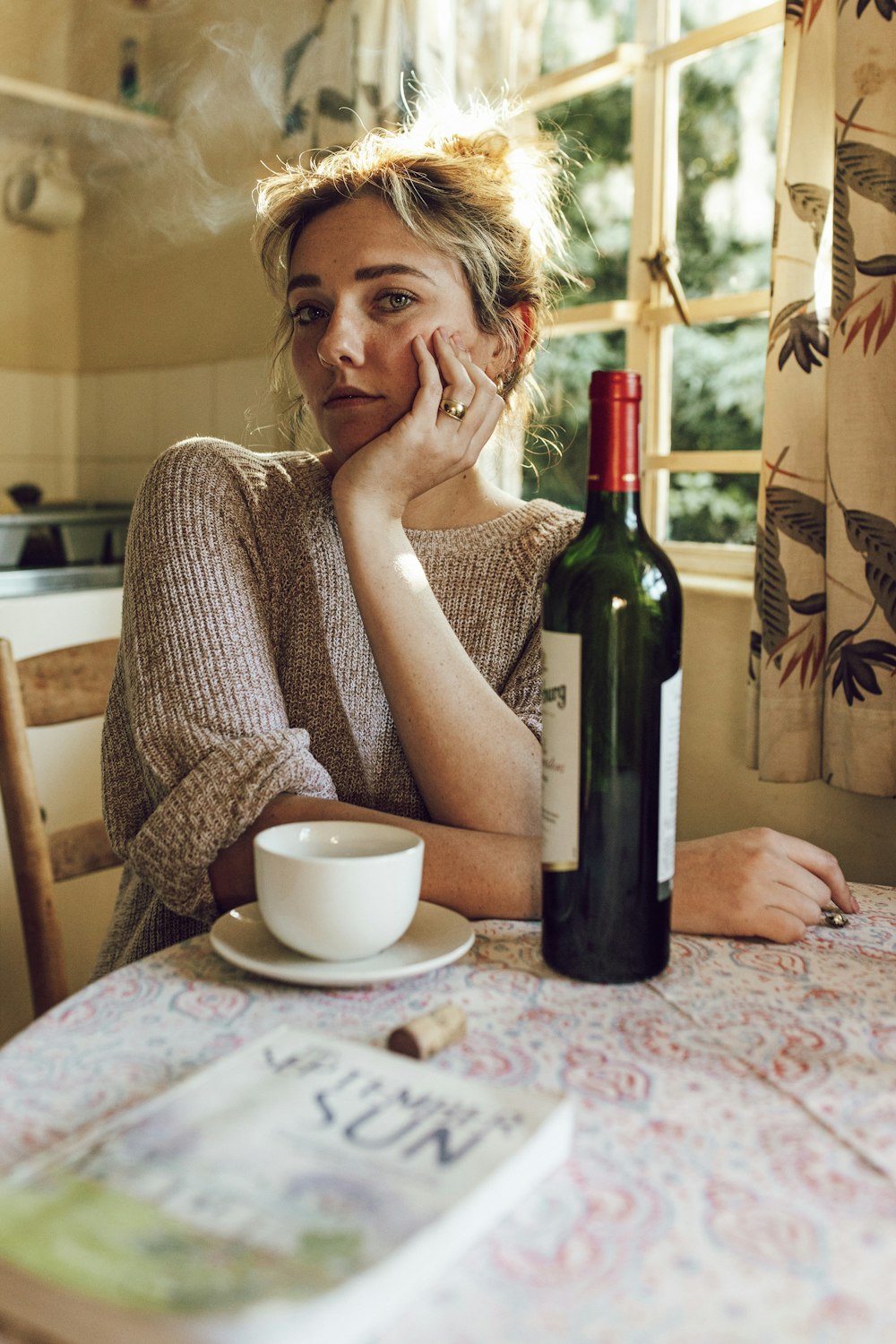 a woman sitting at a table with a bottle of wine