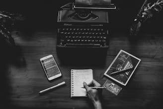a person writing on a notebook next to a typewriter