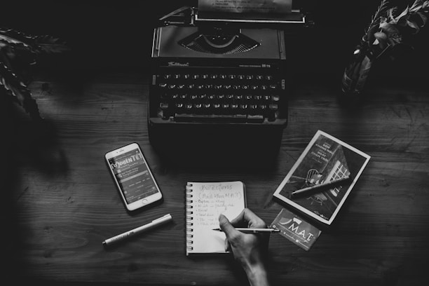 a person writing on a notebook next to a typewriter