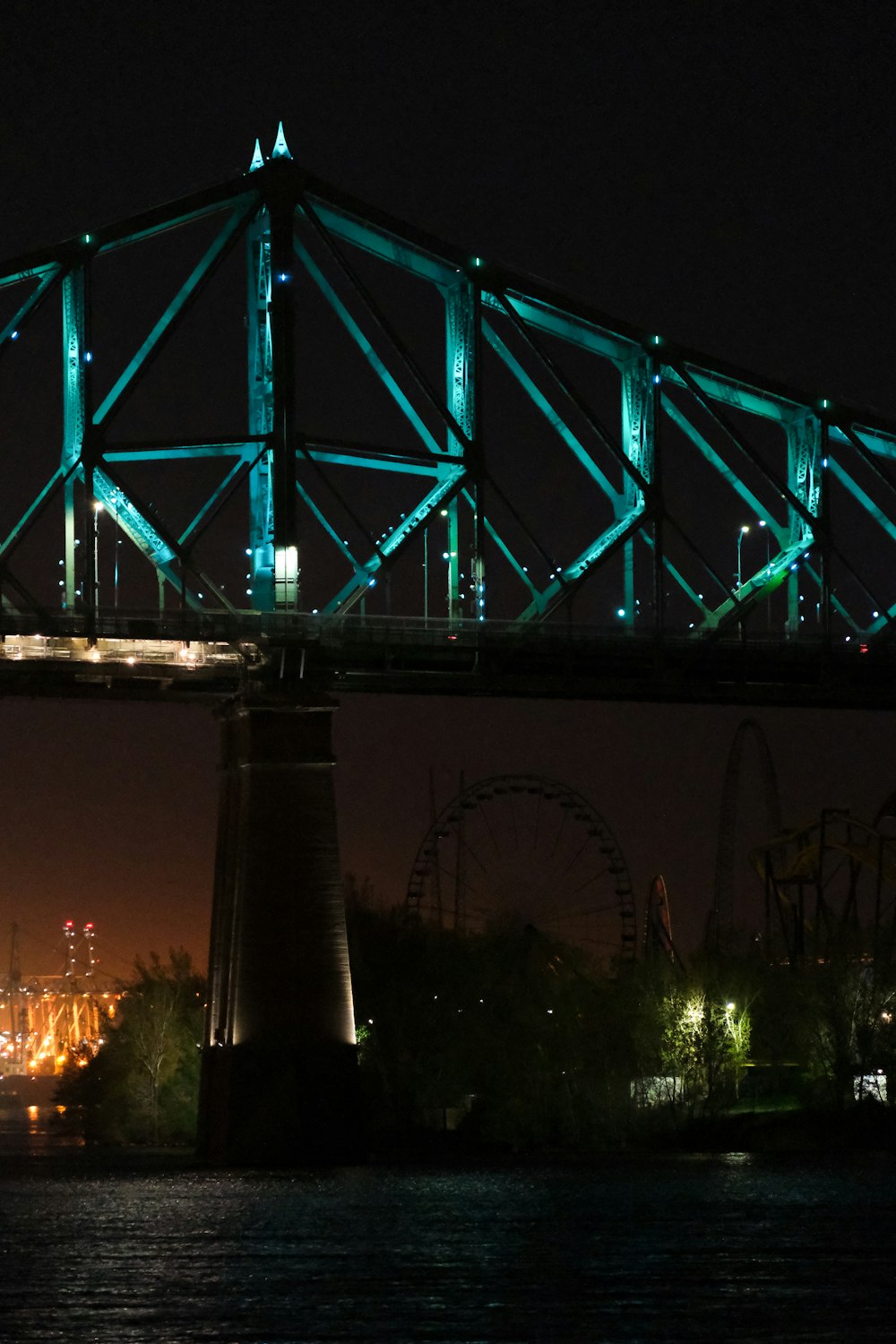 a bridge lit up at night with a ferris wheel in the background