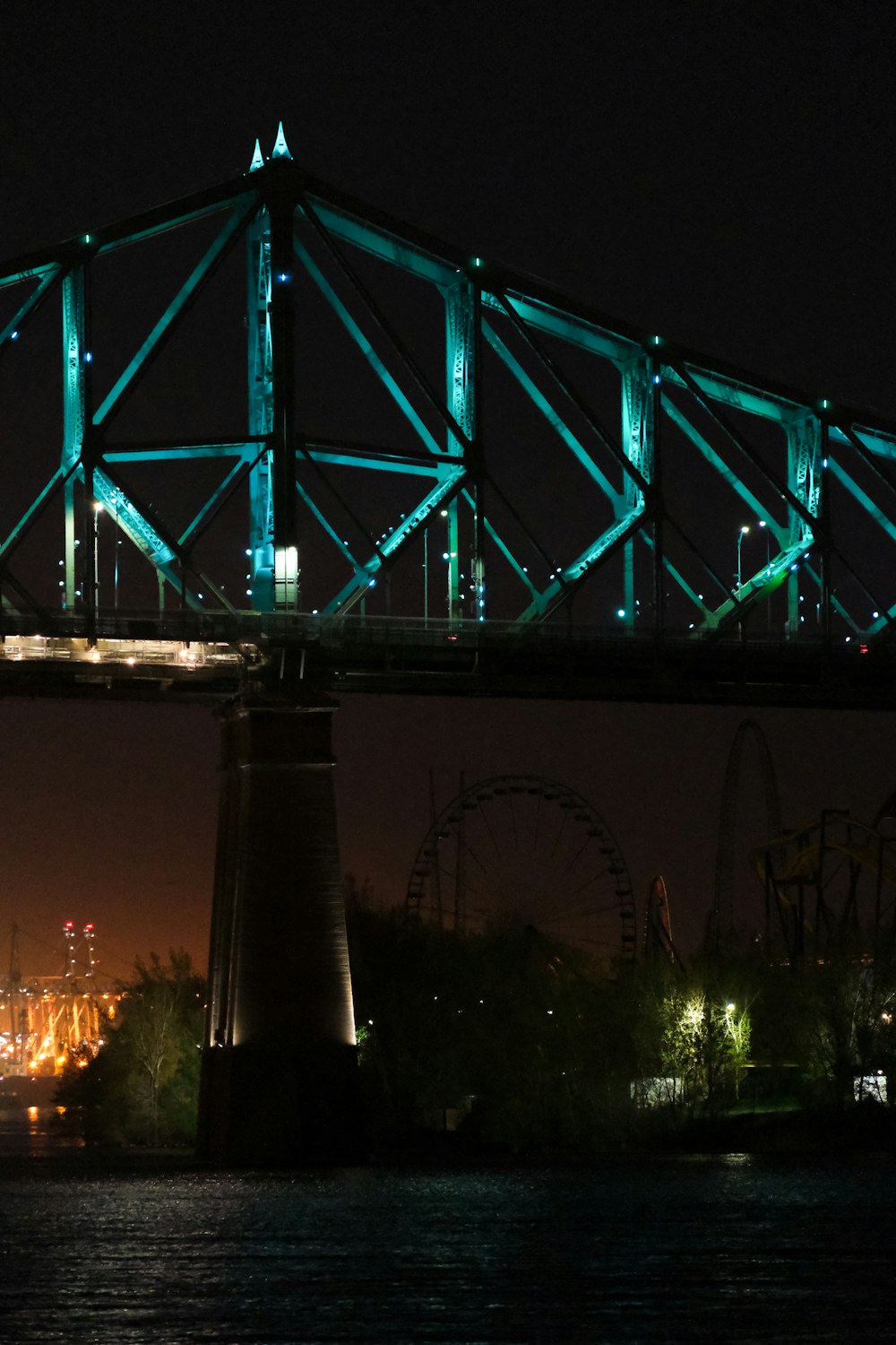 Un puente iluminado por la noche con una noria en el fondo