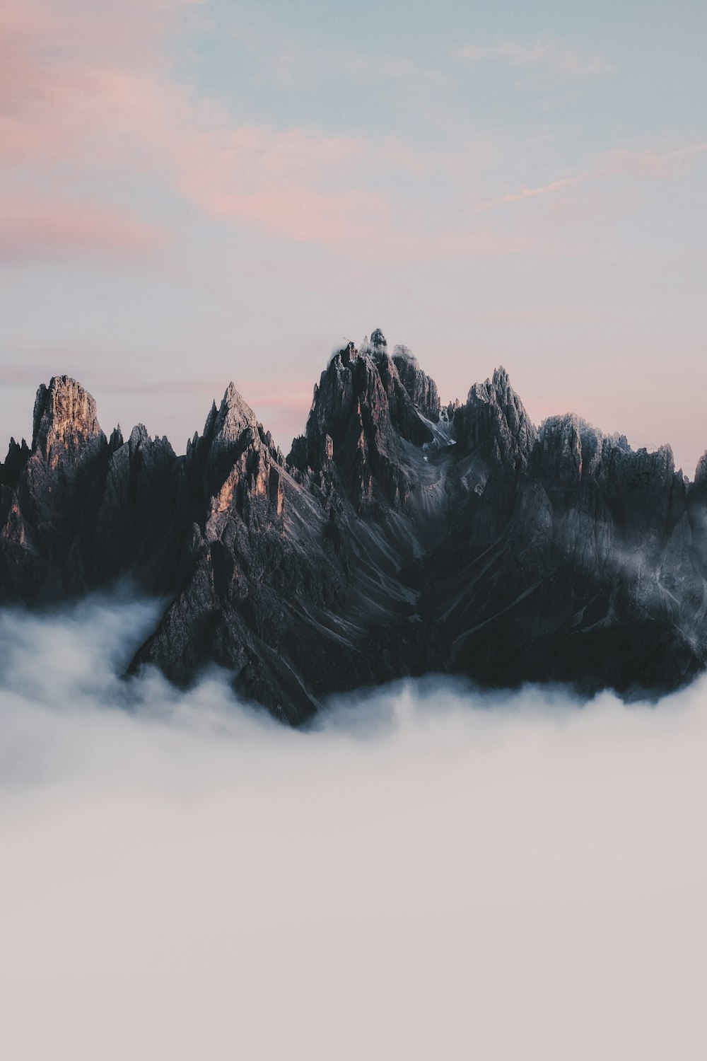 a mountain covered in clouds under a pink sky