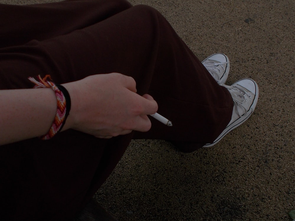 a person sitting on the ground with a cigarette in their hand