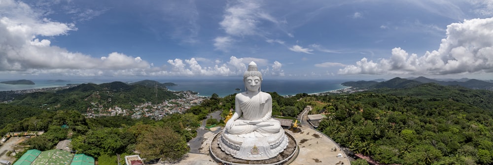 a large white buddha statue sitting on top of a lush green hillside