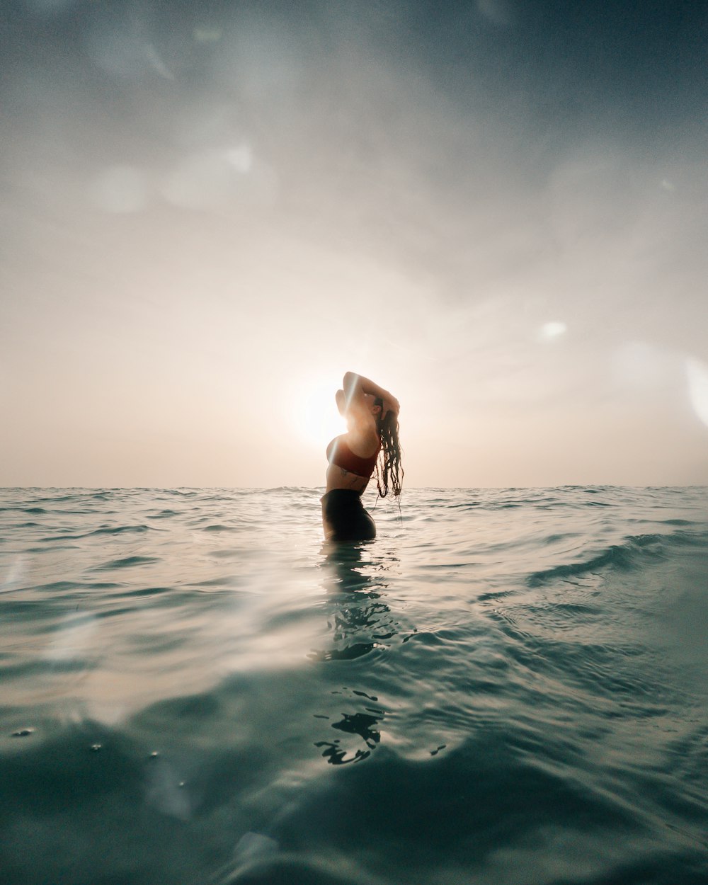 a woman standing in the ocean at sunset