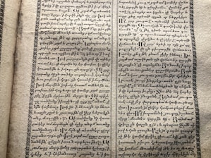 A vintage manuscript page containing two columns of handwritten text on aged paper. The script has a decorative border and is written in an ornate style that suggests historical or ancient content.