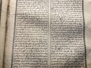 A vintage manuscript page containing two columns of handwritten text on aged paper. The script has a decorative border and is written in an ornate style that suggests historical or ancient content.