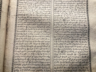 A vintage manuscript page containing two columns of handwritten text on aged paper. The script has a decorative border and is written in an ornate style that suggests historical or ancient content.