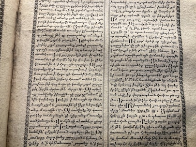 A vintage manuscript page containing two columns of handwritten text on aged paper. The script has a decorative border and is written in an ornate style that suggests historical or ancient content.