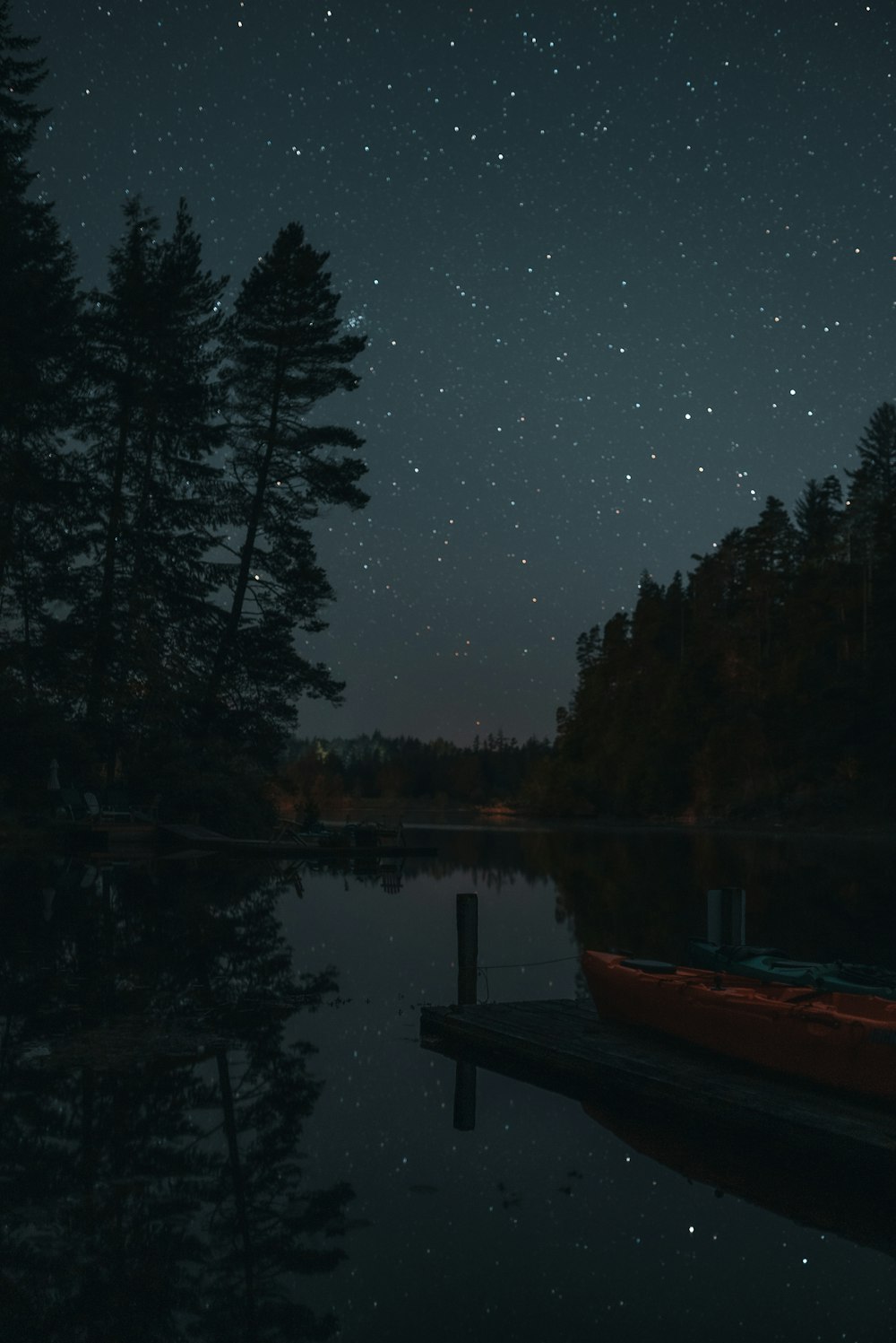 a red canoe sitting on top of a lake under a night sky