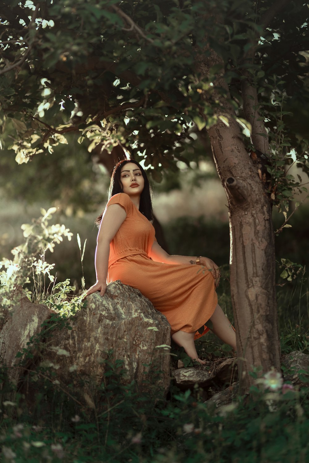a woman in an orange dress sitting on a rock