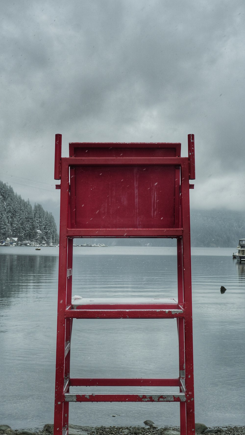 a red lifeguard chair sitting on the shore of a lake