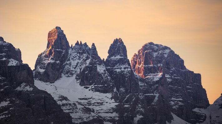 The snow-plastered rock towers of the Brenta Dolomites lit orange by alpenglow above Madonna di Campiglio