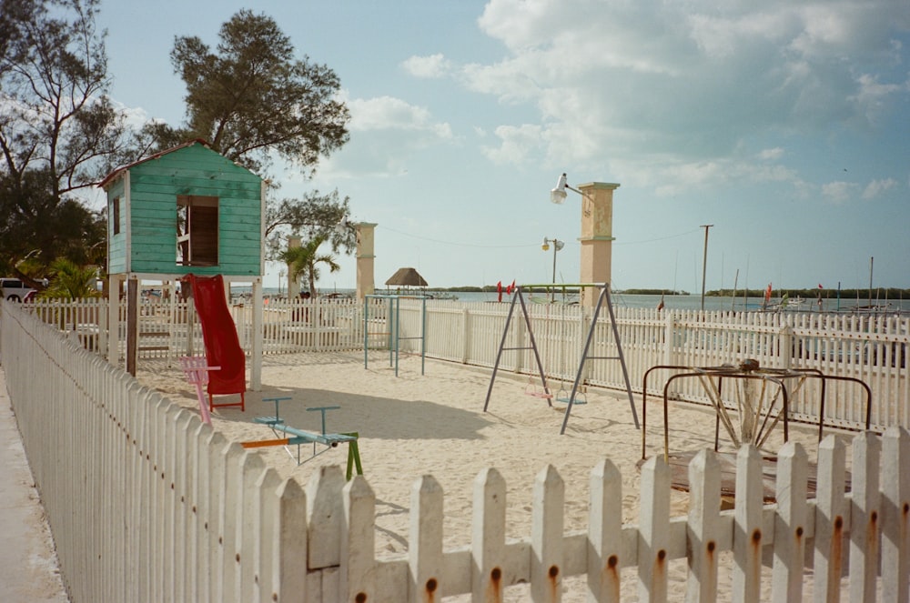 a sandy playground with a red slide and a blue house