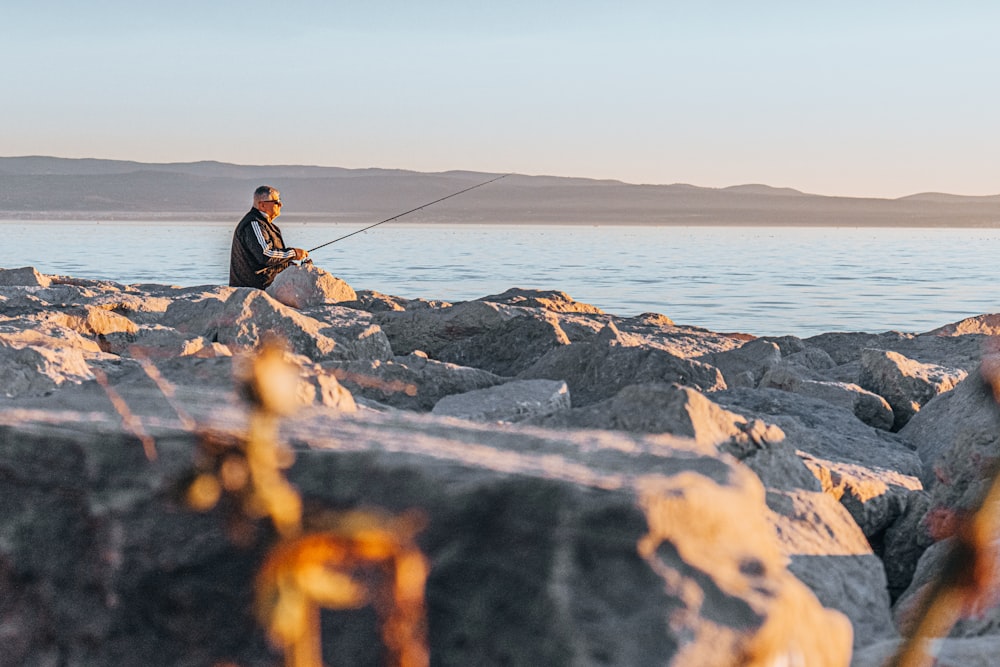 a man sitting on rocks fishing on a lake