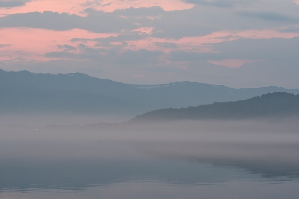 a foggy lake with mountains in the background