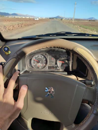 Close-up of hands on a steering wheel with a scenic Canterbury countryside backdrop.