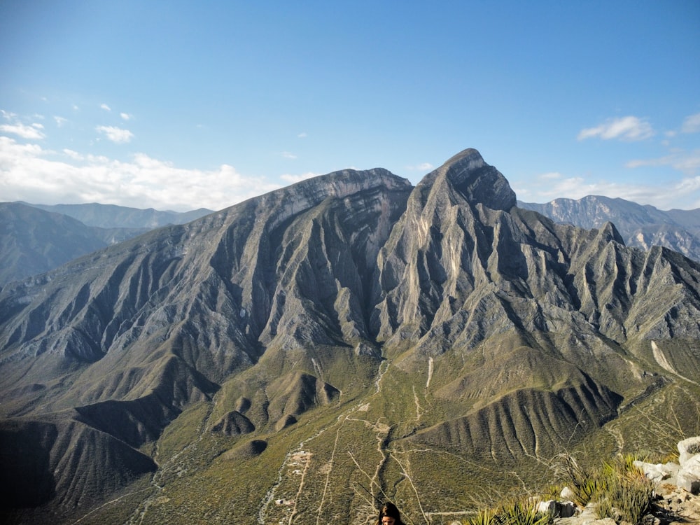 a man standing on top of a mountain next to a lush green hillside