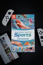 A box of Nintendo Switch Sports is prominently featured, surrounded by various Nintendo Switch controllers and a screen displaying a related interface. The box art depicts animated characters playing sports, such as tennis, with vibrant colors and action-oriented poses.