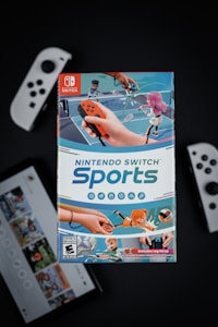 A box of Nintendo Switch Sports is prominently featured, surrounded by various Nintendo Switch controllers and a screen displaying a related interface. The box art depicts animated characters playing sports, such as tennis, with vibrant colors and action-oriented poses.