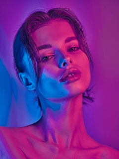 A portrait of a person lit with vibrant neon lighting in shades of pink and blue. The lighting creates a dramatic and artistic visual effect, highlighting the contours and features.