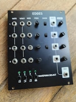 A black audio synthesizer module titled 'EDGES' with multiple knobs and inputs labeled for controls such as GATE, V/OCT, MOD, FREQ, XMOD, OUT, LEVEL, and MIX. There are four sections indicated by numbers 1 to 4 and additional LEDs for waveform selection. The module is placed on a wooden surface.