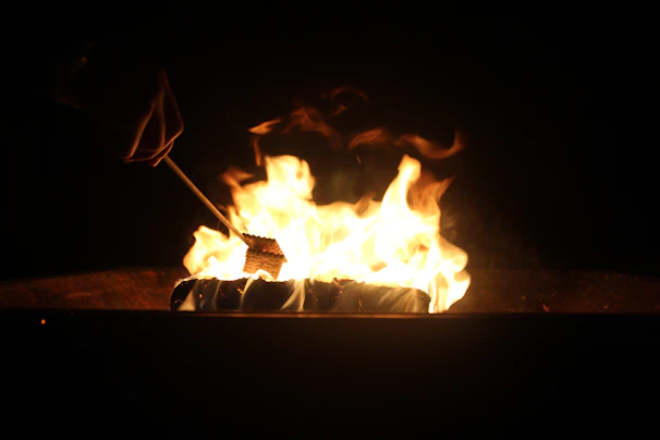 A portable camping stool next to a crackling campfire with marshmallows roasting