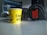 A yellow paper cup with the words 'Chai Kafi' printed on it is placed on a table next to a pair of black JBL headphones. The background is slightly blurred, suggesting an indoor setting, possibly an office or studio environment.