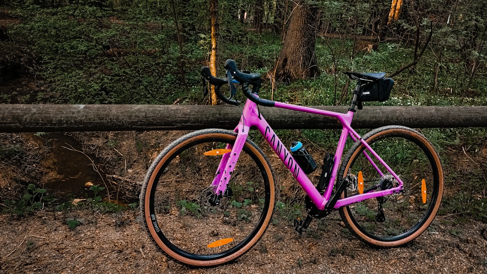 a pink bike parked next to a log in the woods