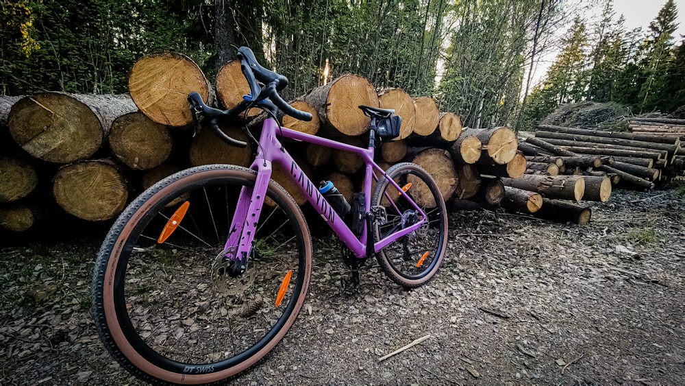 a purple bike parked next to a pile of logs