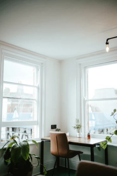 a room with a desk, chair and two windows